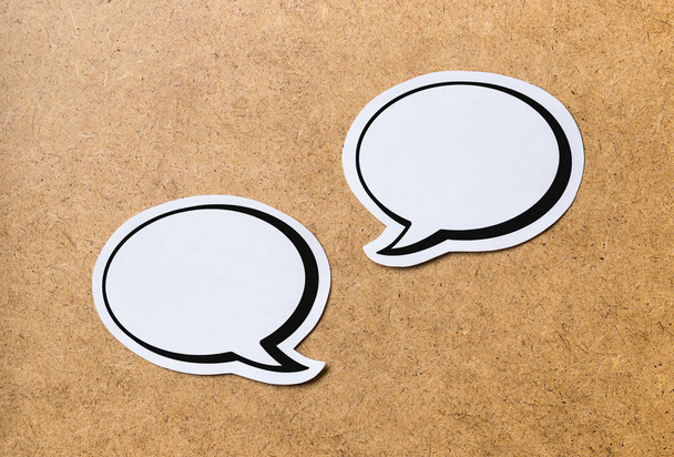 2 blank speech bubbles on a light brown wooden cork board background. Chat bubble cut from paper and cardboard.  - Photo, Image