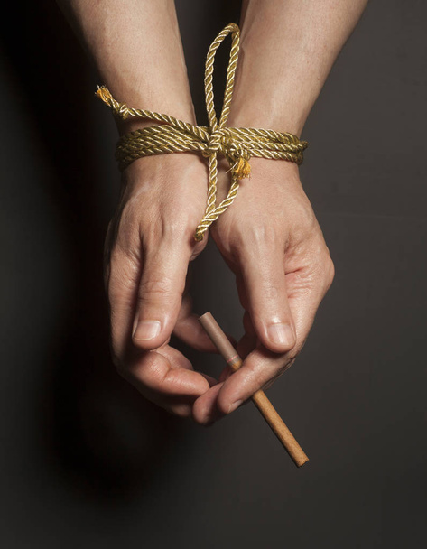A dohányfüggőség. Cigaretta a férfi kezét, egy kötelet kötve. - Fotó, kép