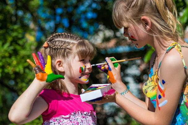 Little happy sisters play with colors in the park, children paint each other  - Photo, Image