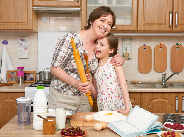 Frau und Kind bereiten auf einem hölzernen Hintergrund Mehl zum Backen und Plätzchen zu. Rohkost und Küchenutensilien. Ein Ei brechen, Teig kochen. - Foto, Bild