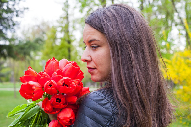 Gorgeous woman with red tulips in the park - Zdjęcie, obraz