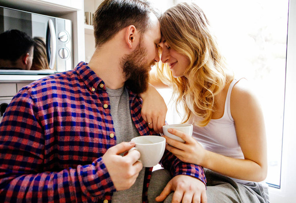 Νεαρό ζευγάρι πίνει καφέ και τσάι στο σπίτι - Φωτογραφία, εικόνα