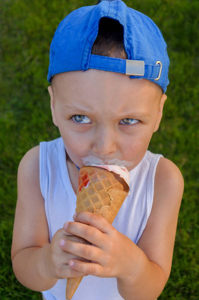 Funny boy in a blue cap eats an ice cream cone  - Photo, Image