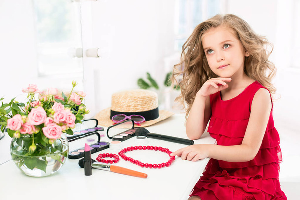 A little girl with cosmetics. She is in mothers bedroom, sitting near the mirror. - Foto, Bild
