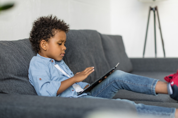 niño reflexivo utilizando la tableta digital en el sofá
 - Foto, imagen