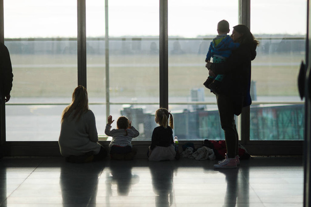 Взрослые и дети сидят у большого окна в аэропорту
. - Фото, изображение