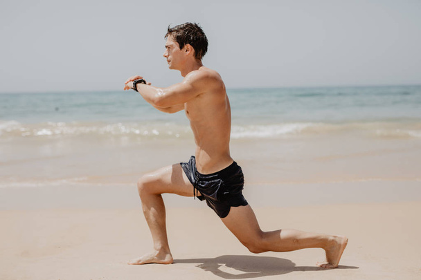 Активний спортсмен біжить на піщаному пляжі. Чоловік довго стрибає в океані, спринтуючись з високою енергією в тренуваннях на відкритому повітрі
. - Фото, зображення