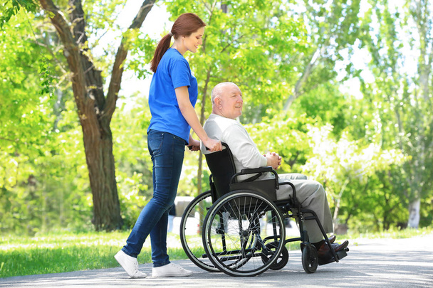 Happy senior man on wheelchair with young female volunteer outdoors - Φωτογραφία, εικόνα