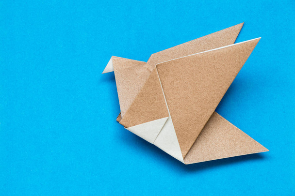 Bruin origami papier in de vorm van de vogels vliegen op blauwe achtergrond - Foto, afbeelding