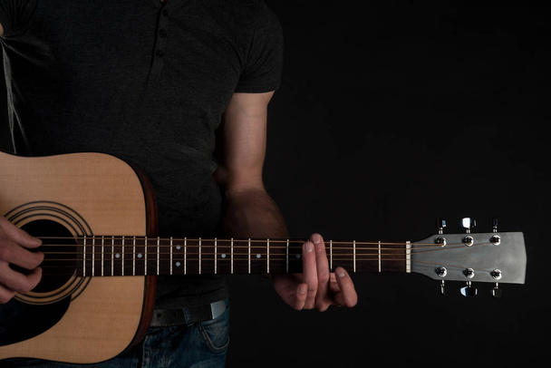 Ακουστική κιθάρα στα χέρια αρσενικό, πάνω σε μαύρο φόντο απομονωμένες. Οριζόντιο πλαίσιο - Φωτογραφία, εικόνα