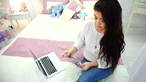 De brunette meisje die zich bezighouden met de financiën en lost geldzaken, zittend op bed in lichte slaapkamer met kerstboom. - Video