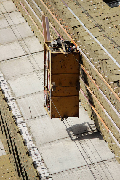 travailleur dans le berceau suspendu jaune monte des panneaux environnementaux pour l'isolation sur un bâtiment de grande hauteur nouvellement construit
 - Photo, image