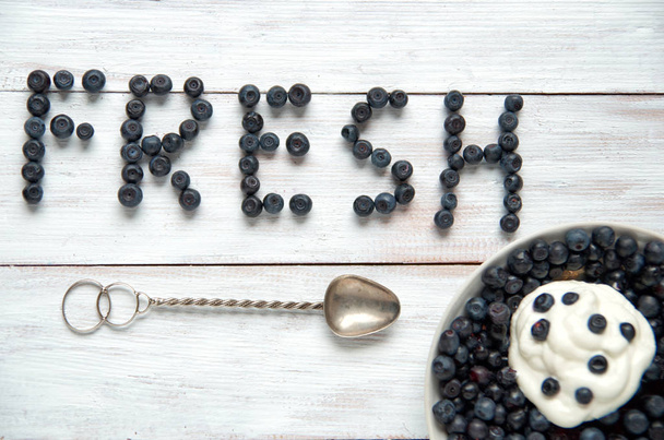 The inscription Fresh of blueberries with plate and vintage silver spoon on white wooden surface - Foto, imagen