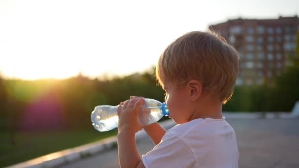 ребенок пьет воду из бутылки на открытом воздухе. Время заката
 - Кадры, видео