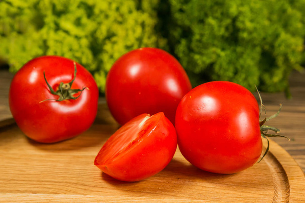 Fresh ripe tomatoes on a wooden table with a green salad on the background. Fresh vegetables close up - Foto, Imagem