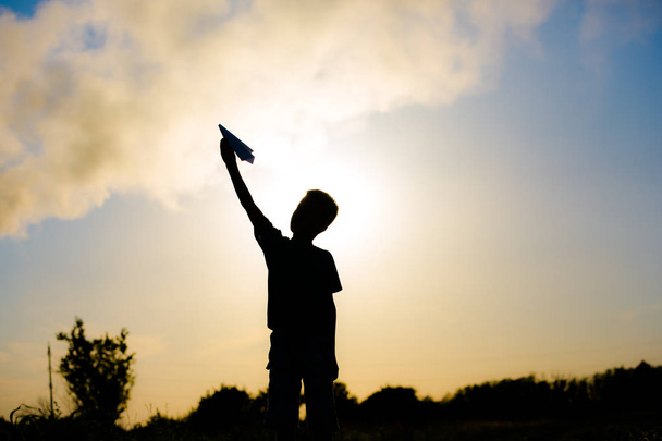 A happy child is playing with a paper airplane at sunset. Classes with children outdoors. Life style - Photo, Image