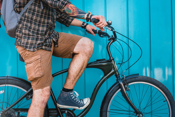 Young Man Cyclist With Tattoo Sitting On Bicycle Near Blue Wall Daily Lifestyle Urban Resting Concept - Фото, изображение