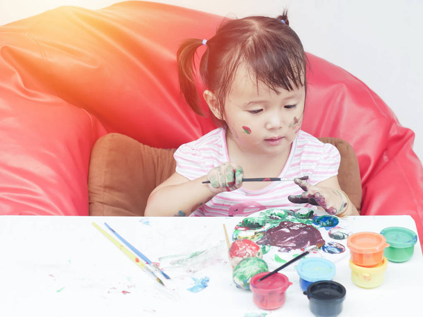 Little Girl Painting with paintbrush and colorful paints by finger hand paint color ,unlimited boundless imagination through Colorful coloring posters blended on desk.children development concept - Foto, imagen