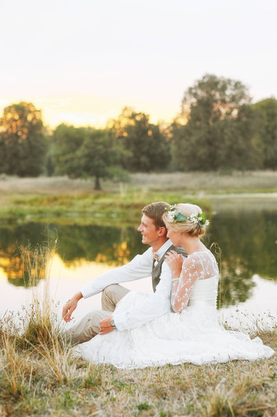 The bride and groom sit by the lake and look at the sunset - Foto, immagini