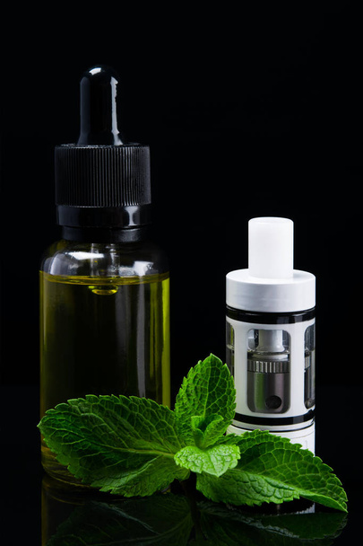 A white tank for an electronic cigarette stands next to a mint fluid - Photo, Image