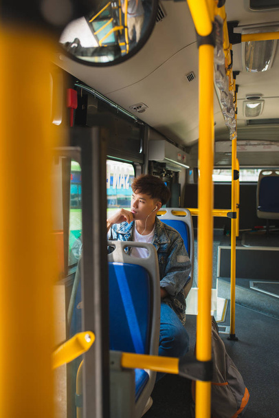 Asian man sitting in city bus, listening to music and looking th - Фото, изображение