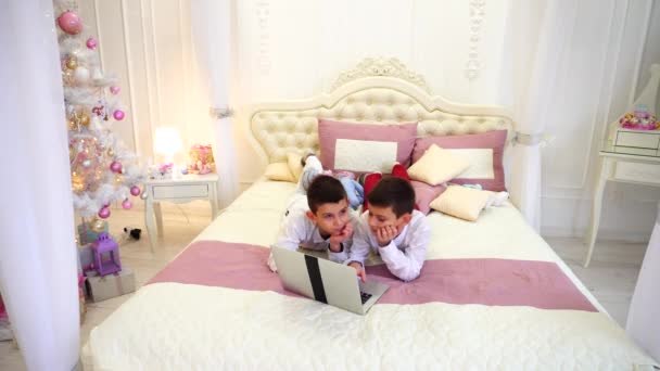 Twee broers kinderen computerspelletjes spelen en ga liggen op bed in lichte kamer met kerstboom overdag. - Video