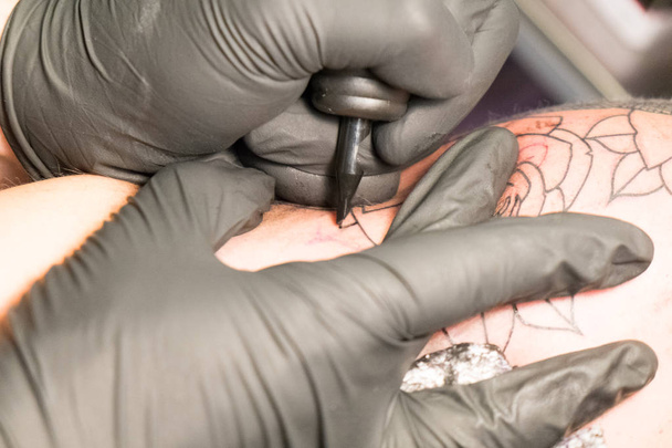 Primer plano de un artista del tatuaje colocando un tatuaje usando su equipo de tatuaje - Foto, Imagen