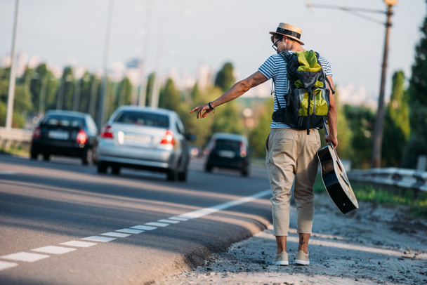 young man with guitar hitchhiking alone - Foto, afbeelding