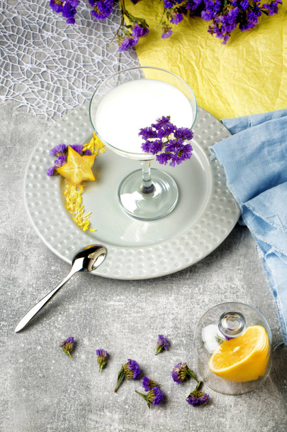 A top view from above a margarita glass filled with fresh, sweet and organic milk beverage on a colorful background. Juicy, ripe lemons and beautiful flowers on a fabric. - Photo, Image