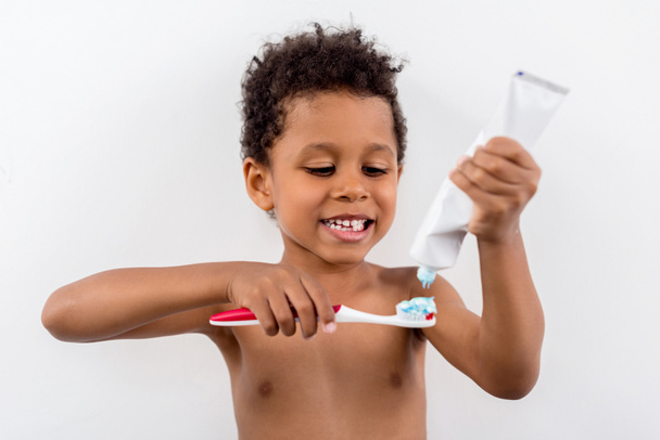 Kind trägt Zahnpasta auf Bürste auf - Foto, Bild