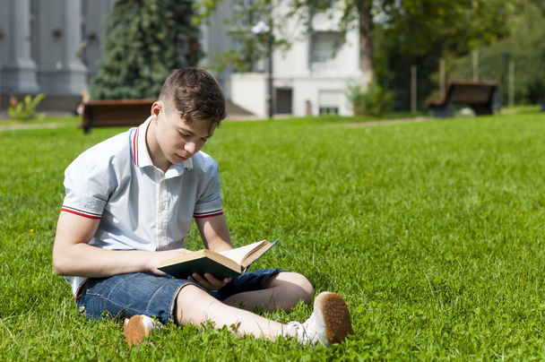 Jongeman lezen van een boek, zittend op het gras - Foto, afbeelding