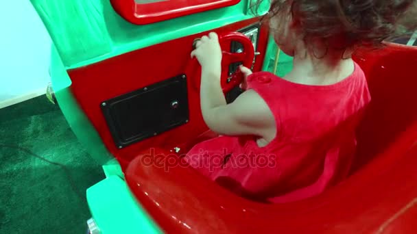 Klein meisje in een rode jurk draait het stuurwiel met de auto - Video