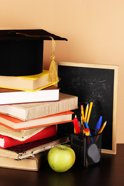 Books and magister cap against school board on wooden table on beige background - Foto, immagini