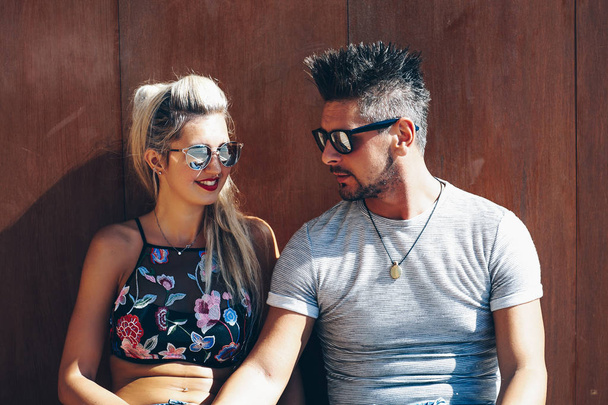 Portrait of handsome couple in casual clothing with sunglasses sitting on wood bench, joyful smiling expressions with heads together. Concept Loving Couple. - Photo, Image