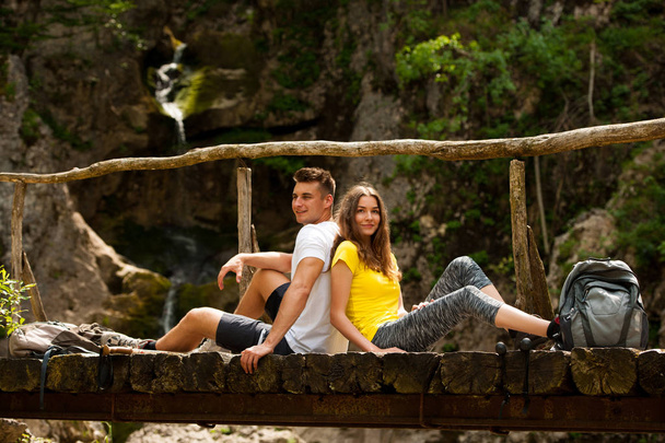 Active couple resting on a wooden bridge over mountain creek  - Foto, Imagen