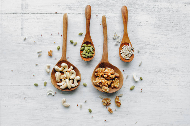wooden spoons with seeds and nuts on the white table - Фото, изображение