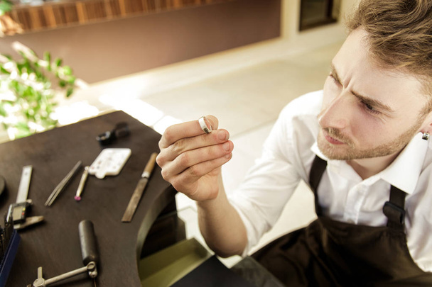 The jeweler holds in his hands and looks at the ring - Foto, Bild