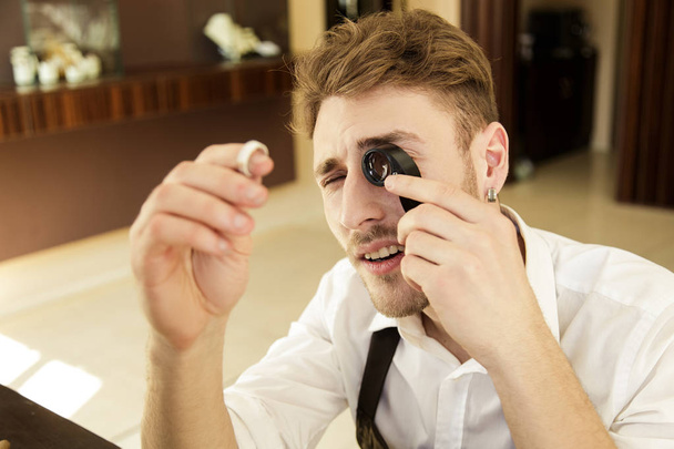 The jeweler holds a ring in his hands and looks at it through a magnifying glass. - Photo, Image