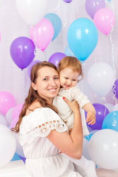 Happy mother hugging her daughter around a lot of colored balloons Isolated on white. - Zdjęcie, obraz