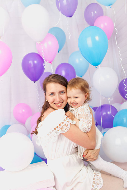 Happy mother hugging her daughter around a lot of colored balloons Isolated on white. - Fotoğraf, Görsel
