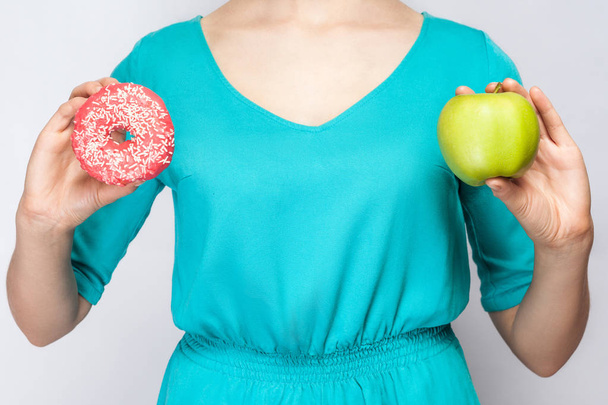 Beautiful young woman in green dress holding apple and donut. studio shot on light gray background - Photo, image