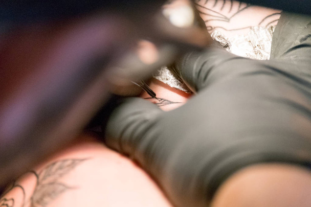 Primer plano de un artista del tatuaje colocando un tatuaje usando su equipo de tatuaje - Foto, imagen