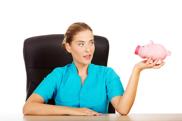 Young female doctor or nurse holding piggybank - Foto, afbeelding