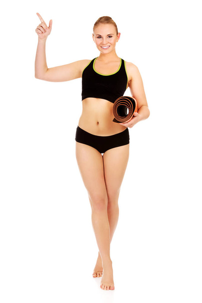 Young athletic woman holding mat and pointing for something - Foto, afbeelding