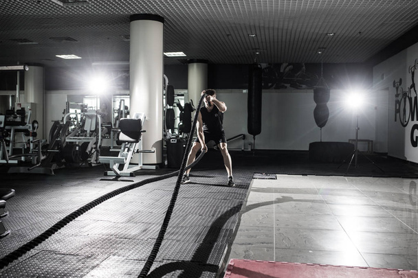 Fitness man working out with battle ropes at gym. Battle ropes fitness man at gym workout exercise fitted body. Fitness man training with battle rope in fitness club. Training with battle rope - 写真・画像
