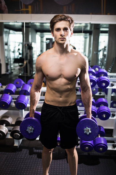 very power athletic guy , execute exercise with dumbbells, in gym hall - Fotografie, Obrázek