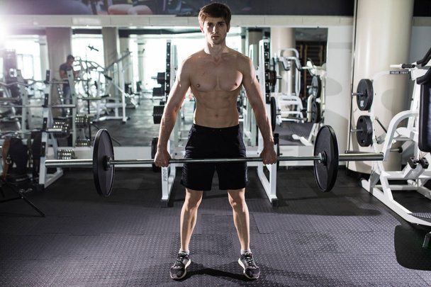 young man flexing muscles with barbell in gym. Sport - Φωτογραφία, εικόνα