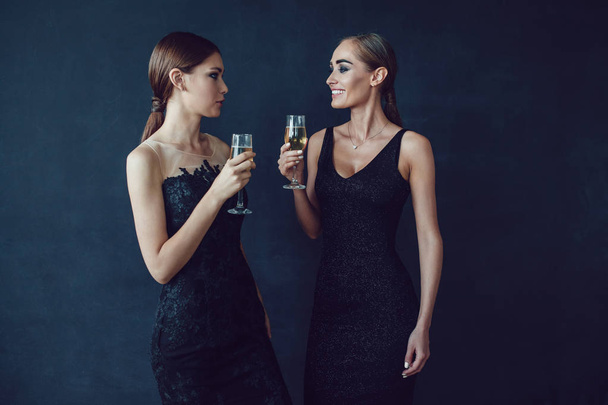 Aantrekkelijke vrouwen in Cocktailjurken houden glazen champagne, praten en lachen. - Foto, afbeelding