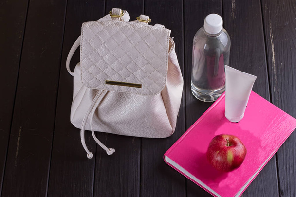 Білий шкіряний рюкзак, рожева книга, пляшка води
 - Фото, зображення