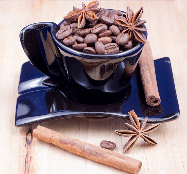 Чорна чашка, наповнена кавовими зернами, анісом та корицею на дерев'яній поверхні
 - Фото, зображення